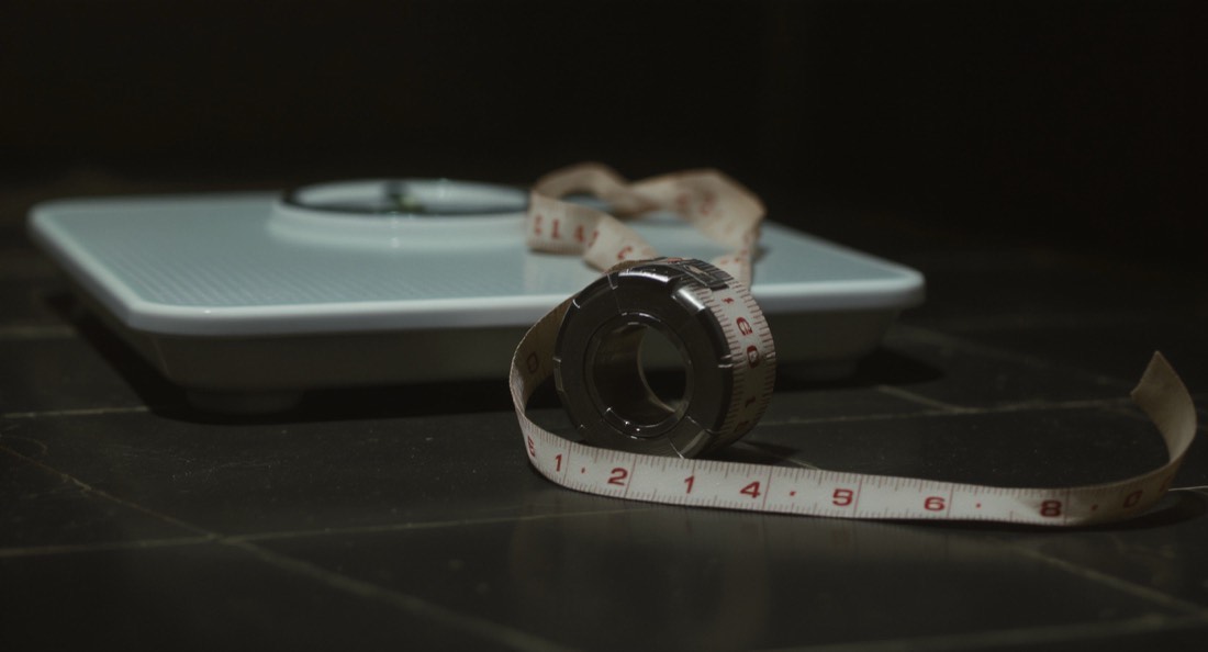 A bathroom scale and a cloth tape measure on a dark tiled floor